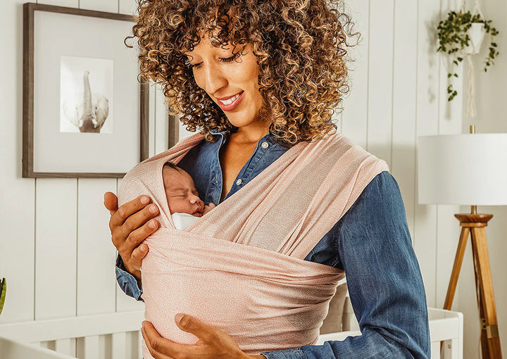 Mom snuggles baby in pink baby wrap carrier in nursery