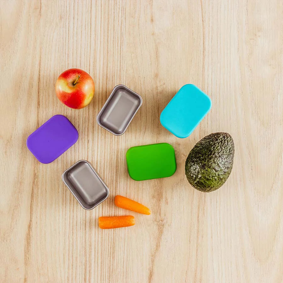 Blue purple and green dip contains on a wooden table with an apple, avocado, and carrots