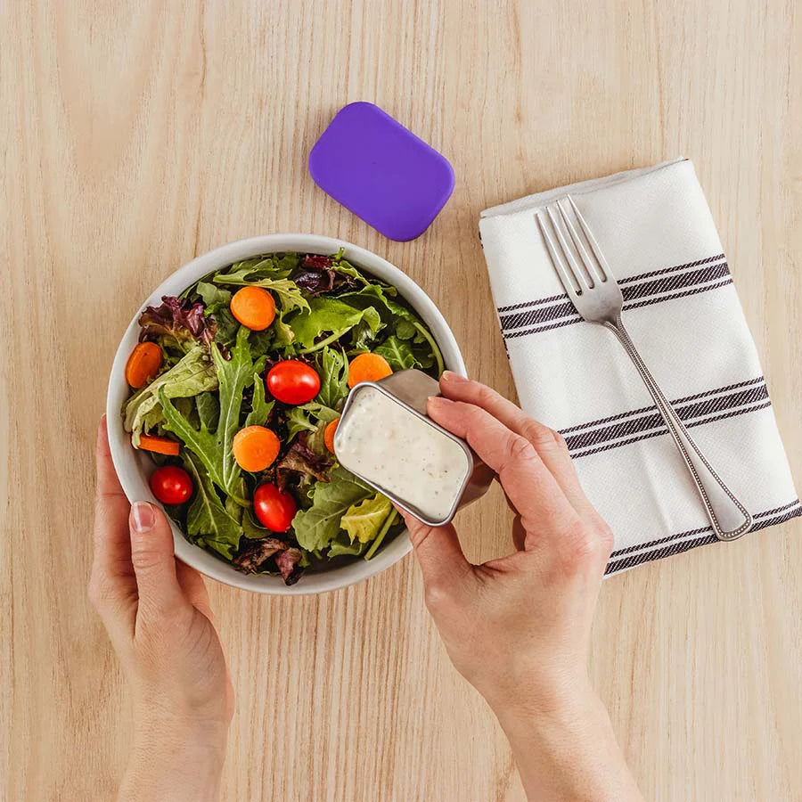 Mom pours dressing out of stainless steel dip container onto a salad in a white bowl