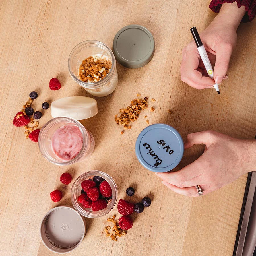 Mom labels glass food storage jars containing fruit, smoothie, granola