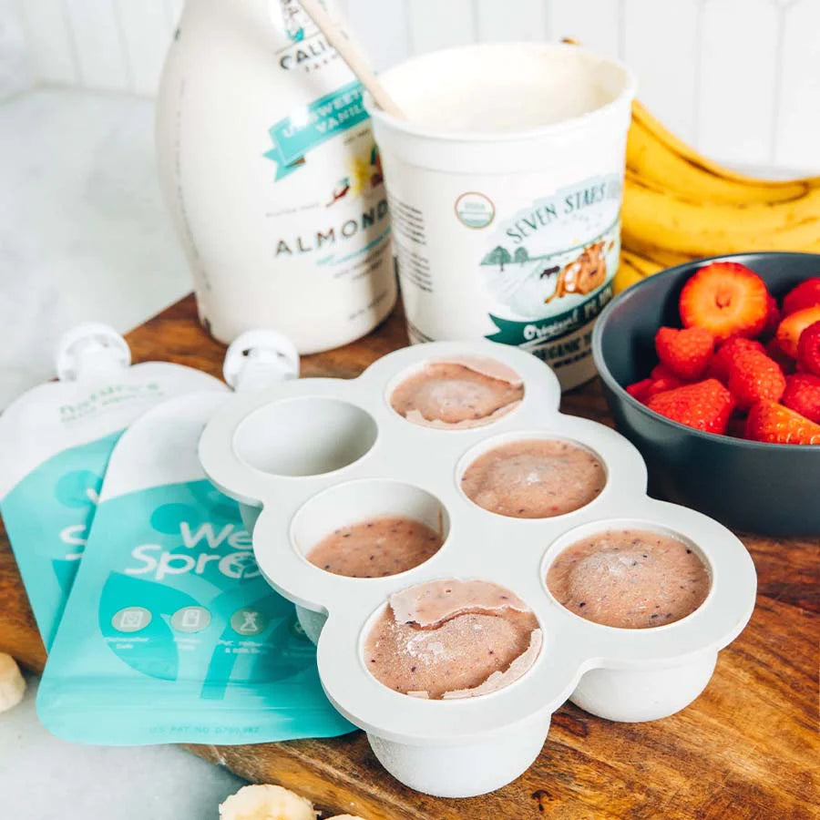Frozen smoothie in freezer mold laid on top of reusable squeeze pouches with bananas and strawberries