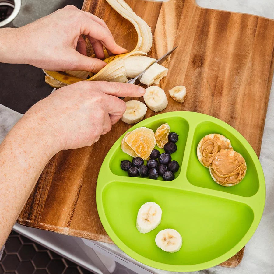 Mom cuts banana next to a green silicone divided plate