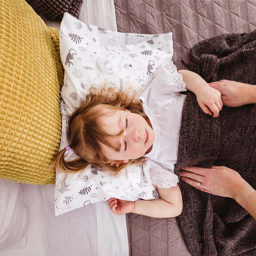 Toddler lays in bed on a toddler pillow in white safari