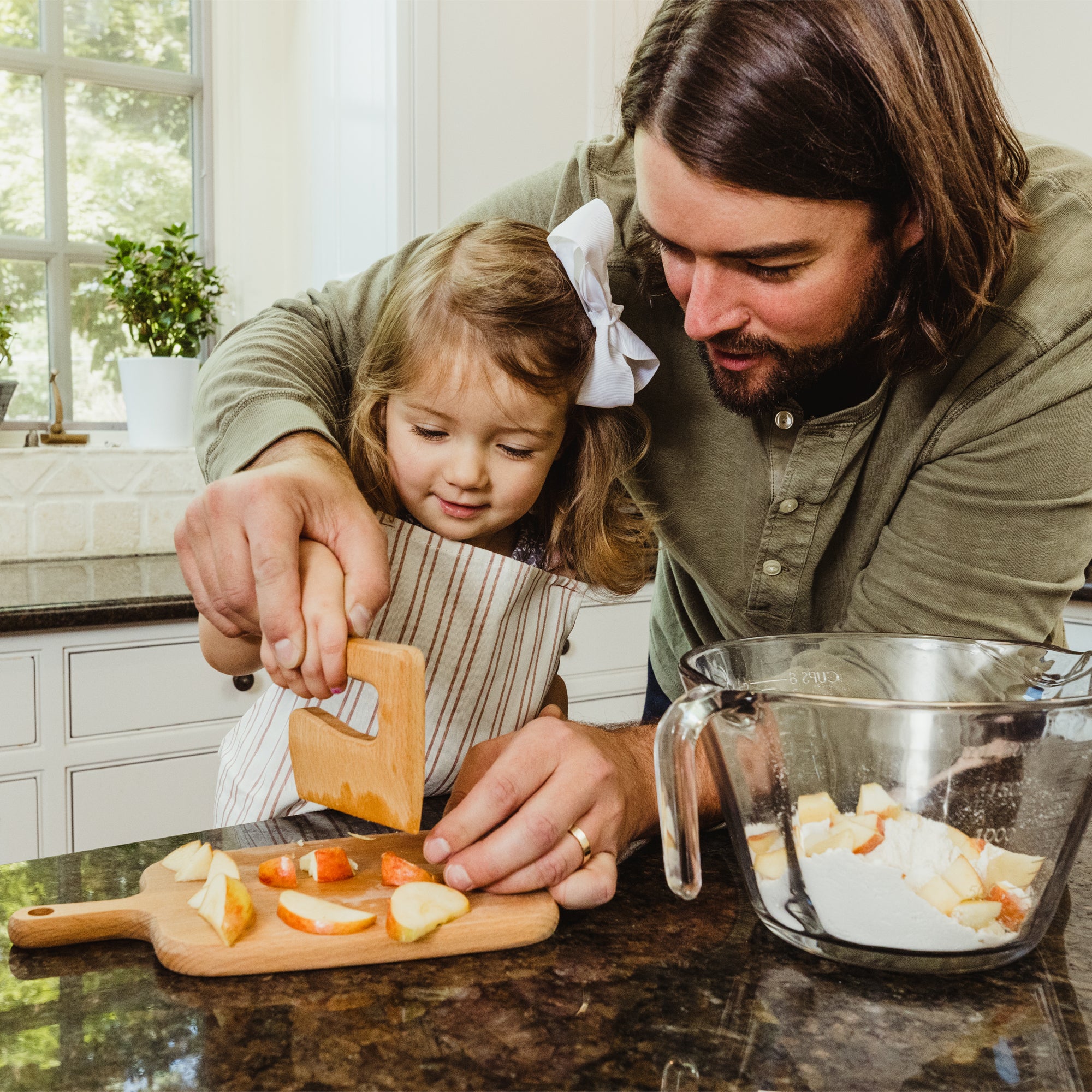 Dad helping daughter chop apples on a cutting board in their kitchen
