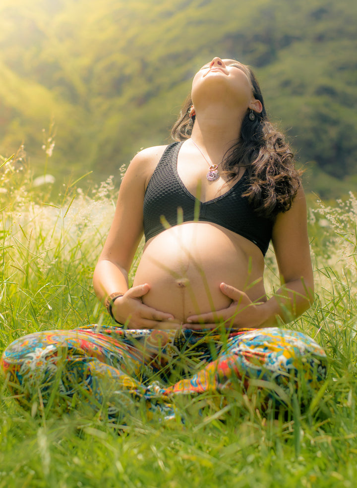 Pregnant women sitting in a field looking up at the sun.
