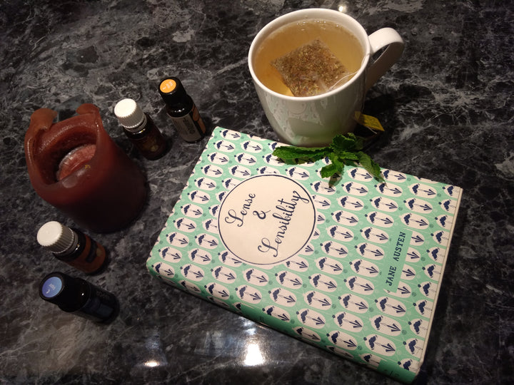 Note book with sense and sensibility written on it surrounded by a cup of tea and a candle