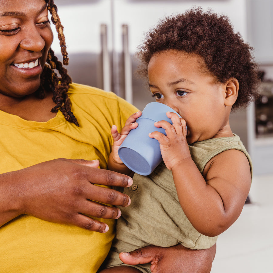 Mom holding son who is drinking out of a blue bamboo sippy cup in kitchen