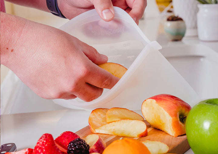 somebody putting sliced fruit into a silicone reusable zipper bag in kitchen