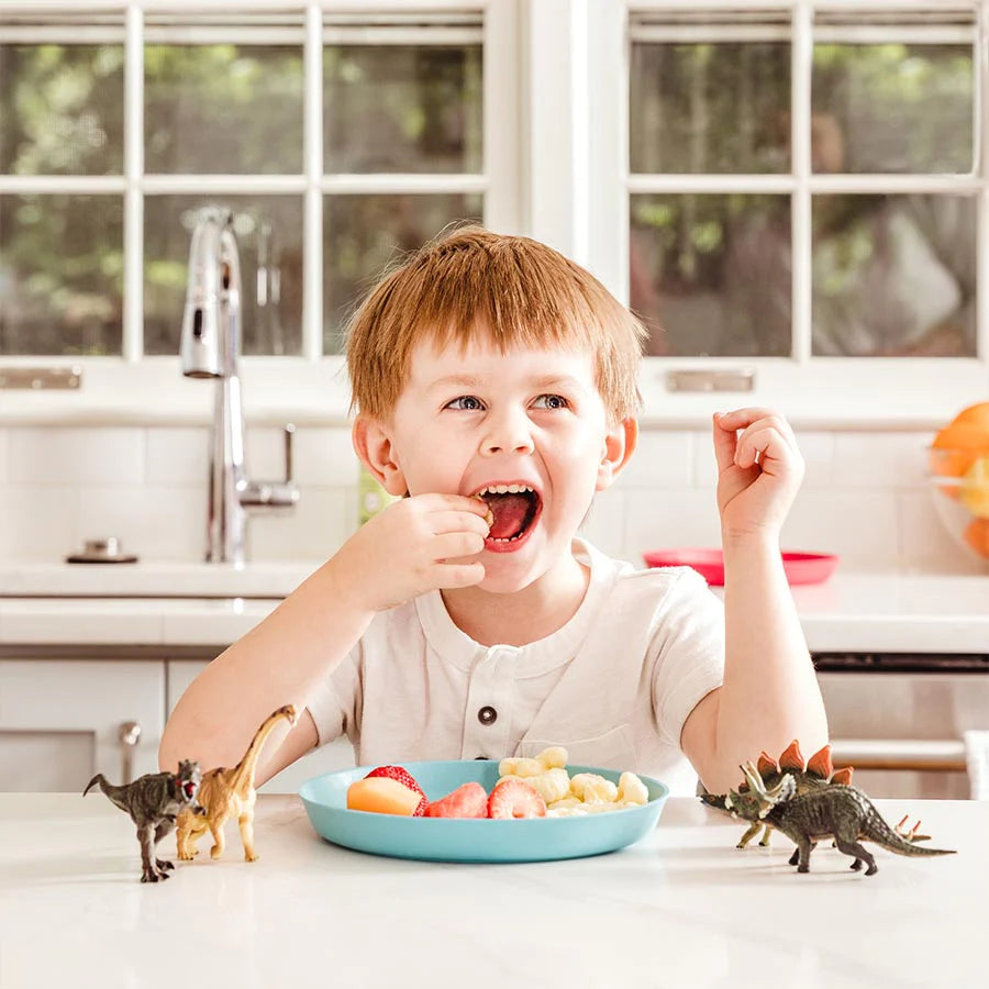Toddler eats fruit as a snack with blue bamboo plate at table