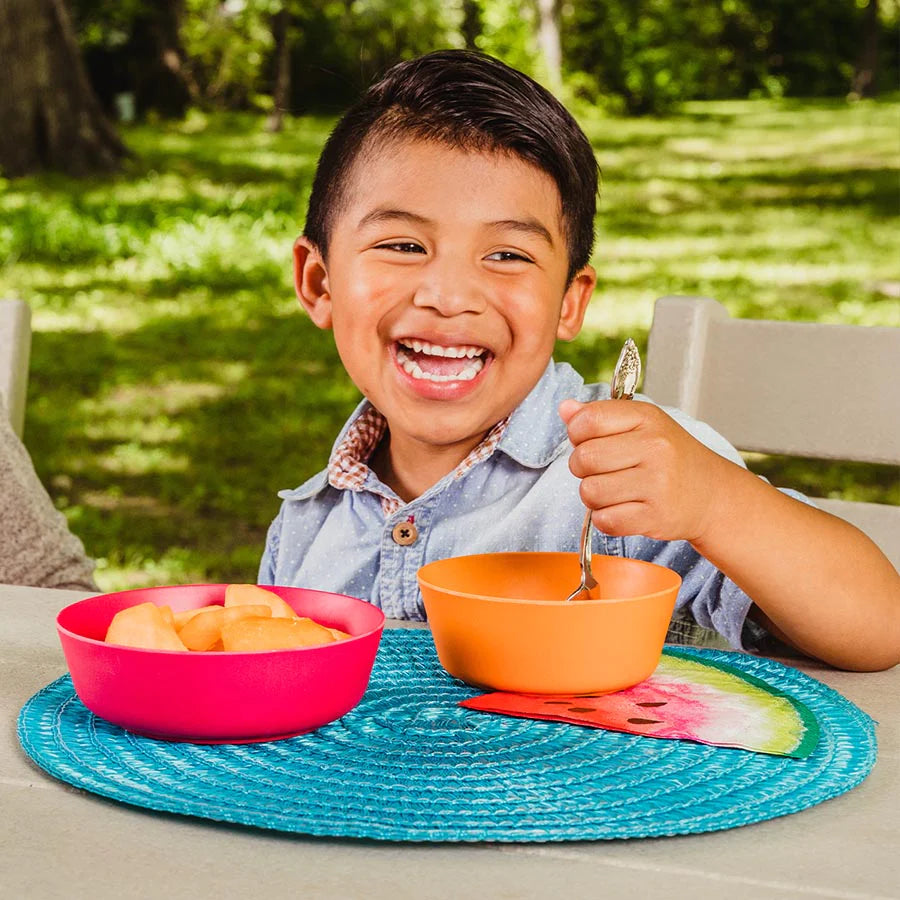 Toddler eats outside from a red and orange bamboo bowl