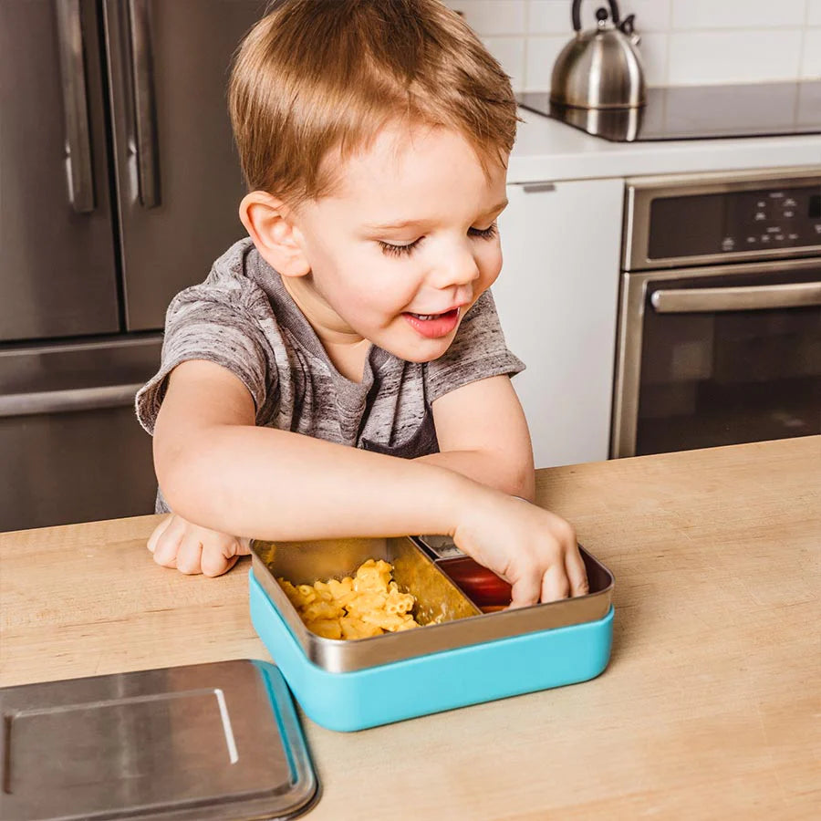 Toddler eats snacks out of blue stainless steel bento box with sleeve