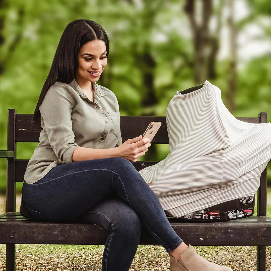 Mom sits on park bench with her baby in a car seat covered car seat