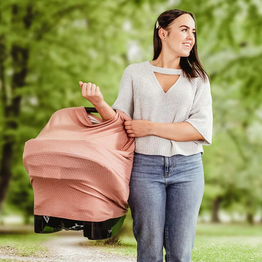 Mom holds baby in car seat with pink car seat cover while walking through the park