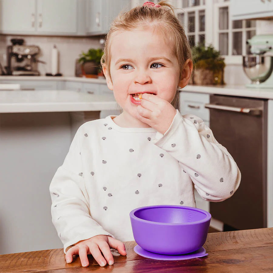 Toddler eats snack at kitchen counter out of purple silicone suction bowl