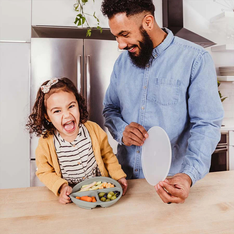 Dad lifts lid off of daughter's gray silicone divided plate with food in it