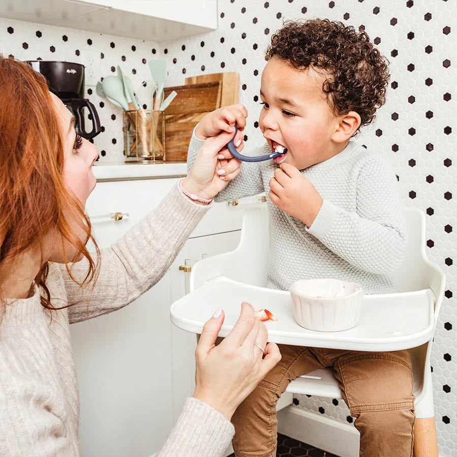 Mom feeds baby with navy silicone baby spoon at high chair