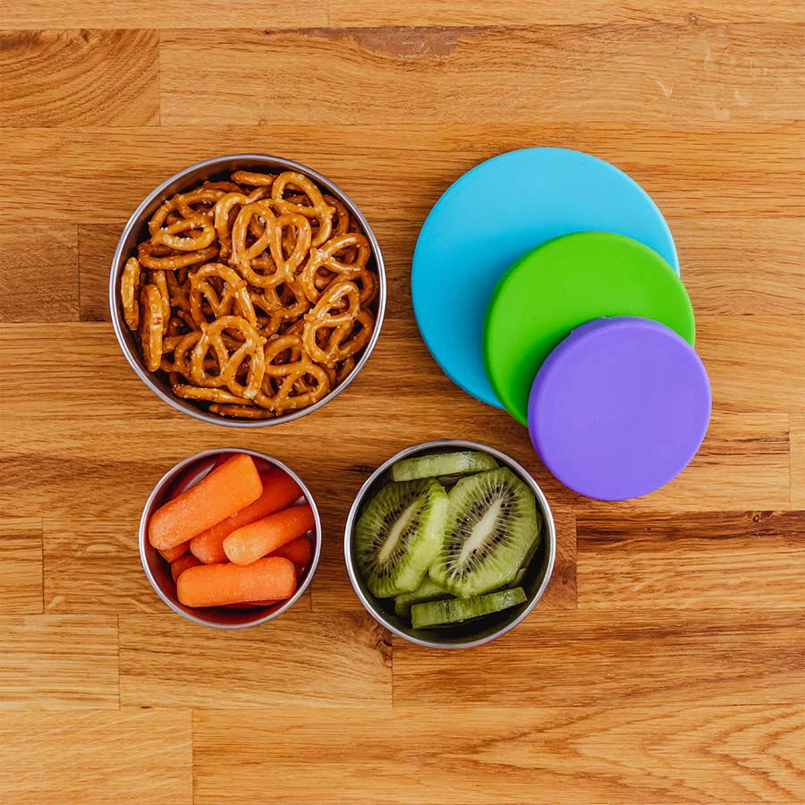 Kiwi, Carrots and pretzel's in purple, green and blue stainless steel storage containers