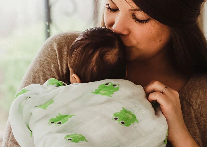 Mom snuggles with baby in frogs fabric swaddle
