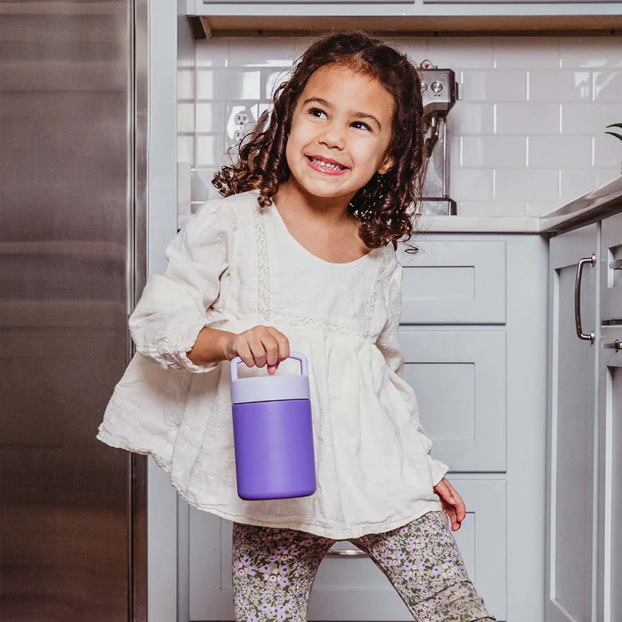 Toddler in kitchen holds a purple thermos 