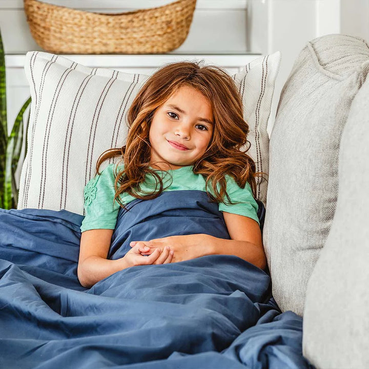 Child lays on couch under navy kids weighted blanket