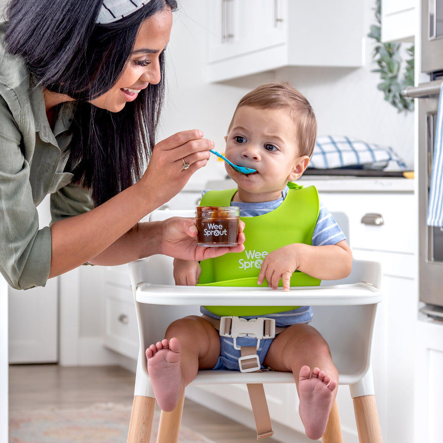 mom feeding child in high chair from a baby food glass storage container